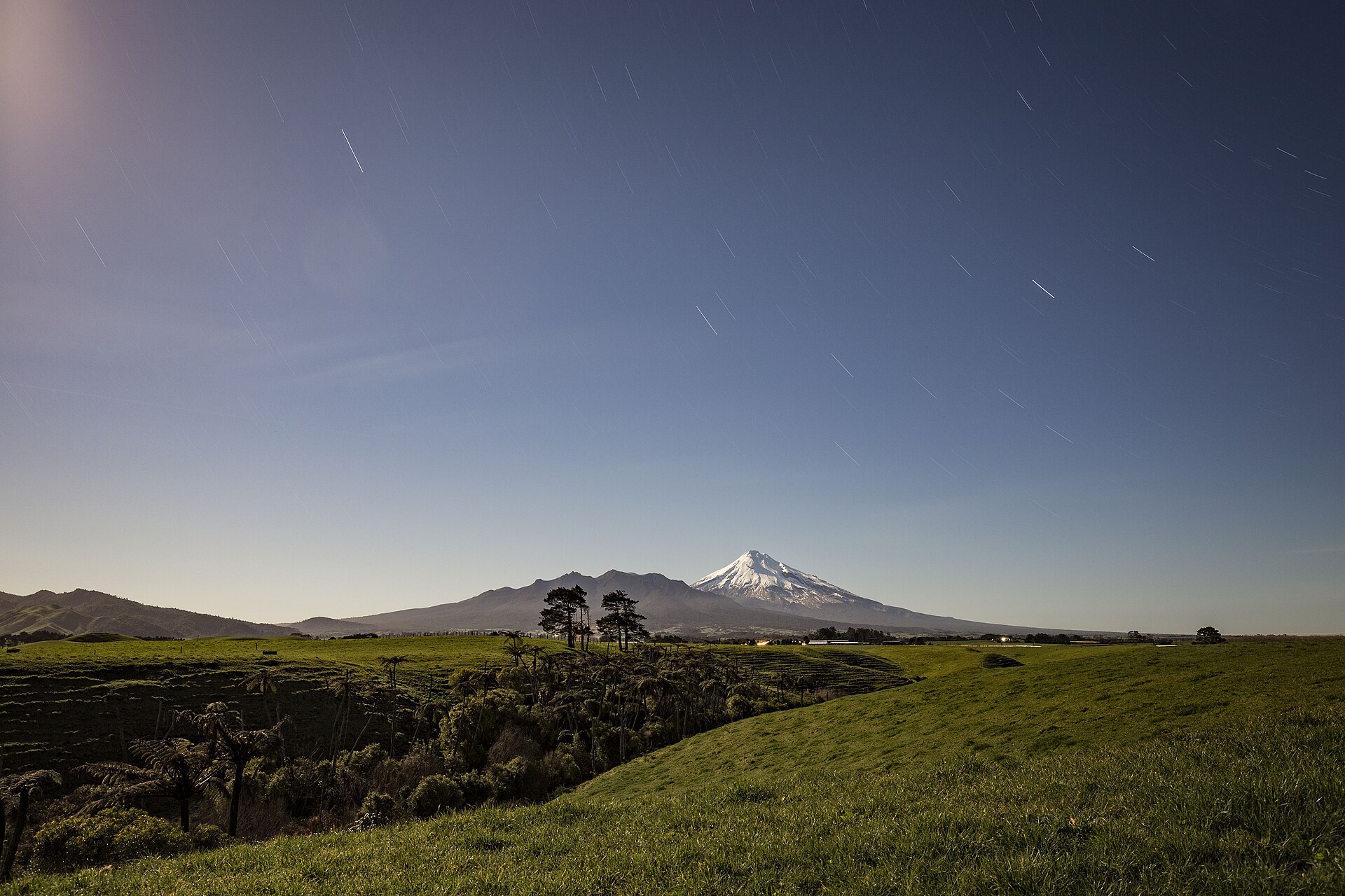 Cielo nocturno con estelas circulares de estrellas sobre la silueta de una colina