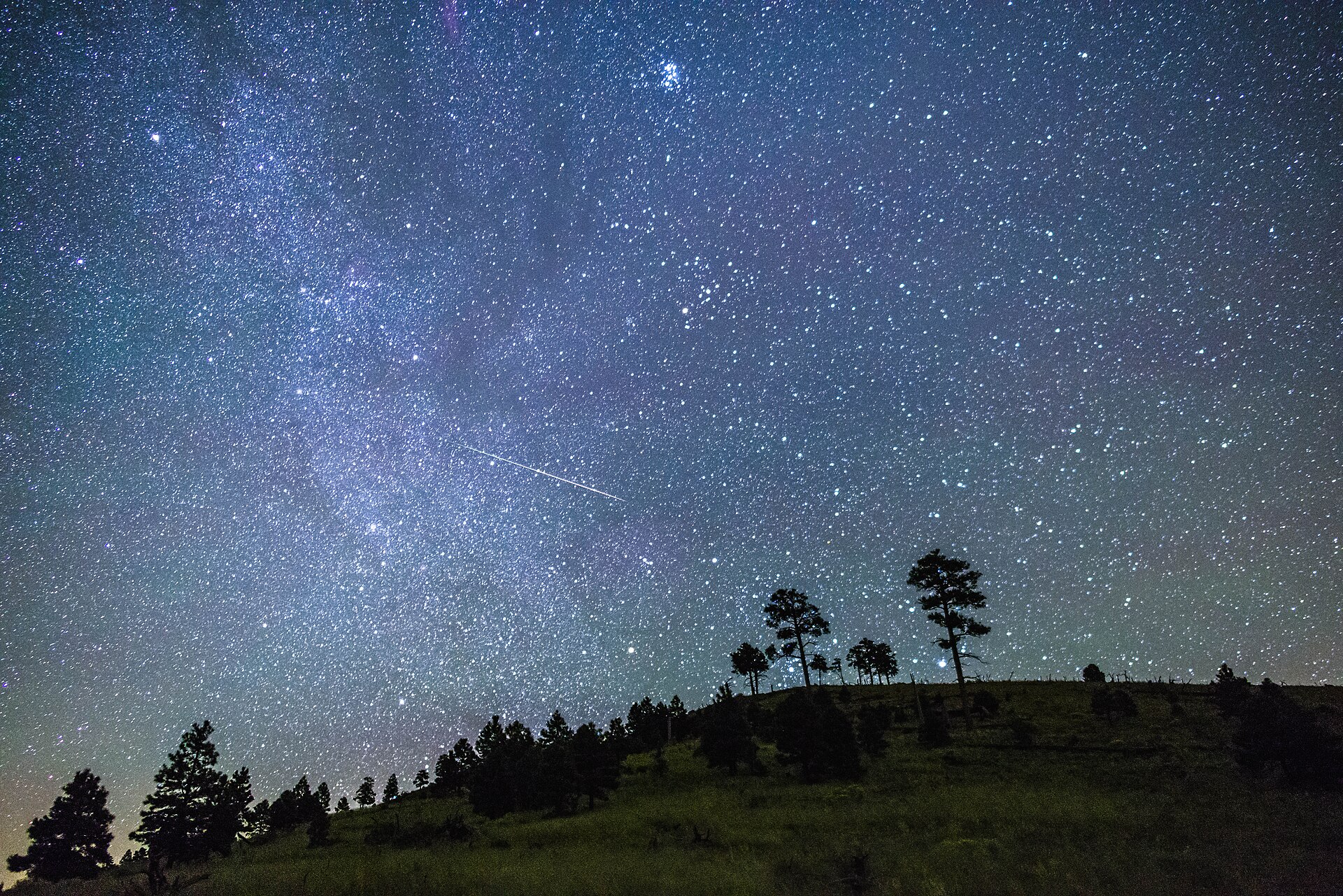 Estela luminosa de un meteoro cruzando un cielo nocturno despejado sobre el horizonte