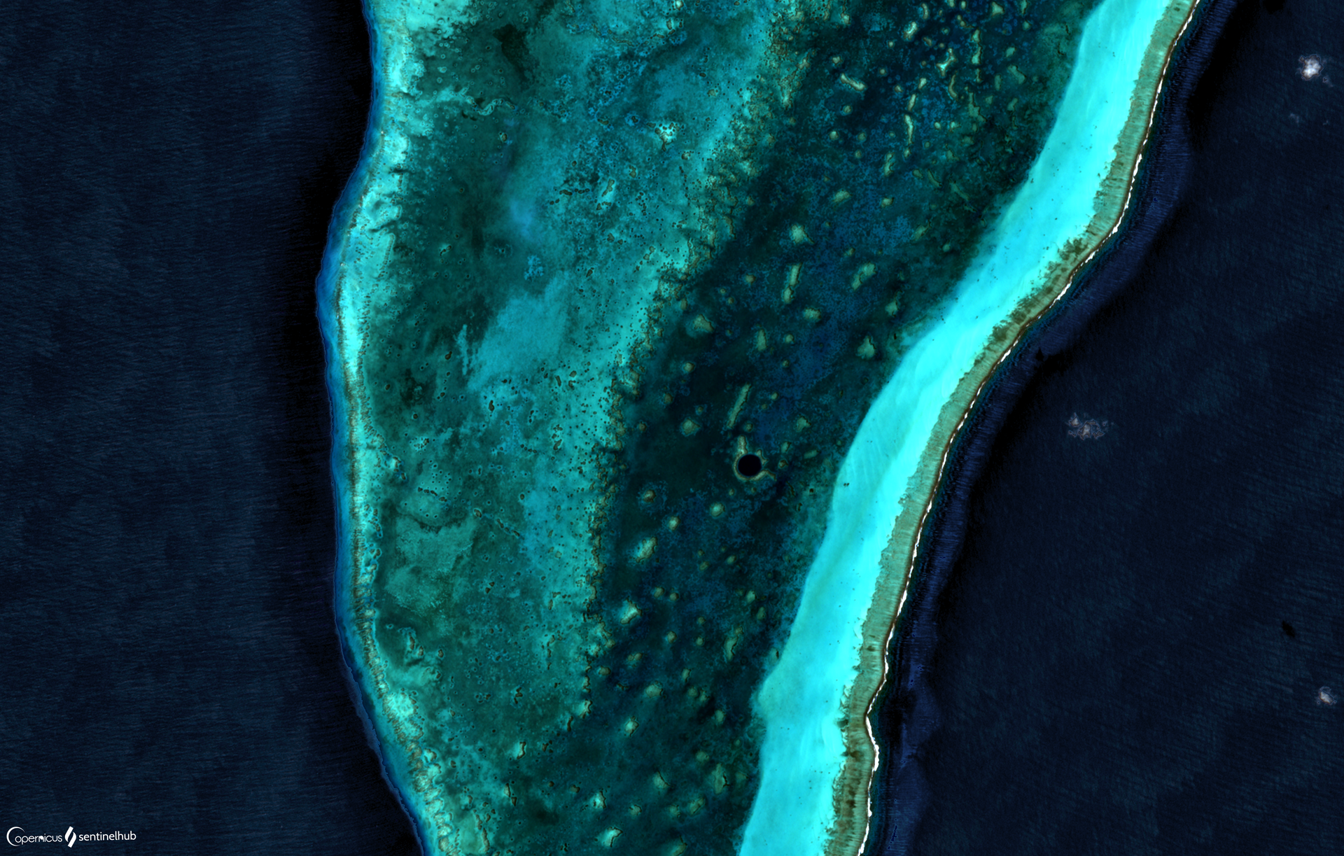 Vista aérea de un círculo de agua azul oscuro rodeado por un arrecife de aguas claras