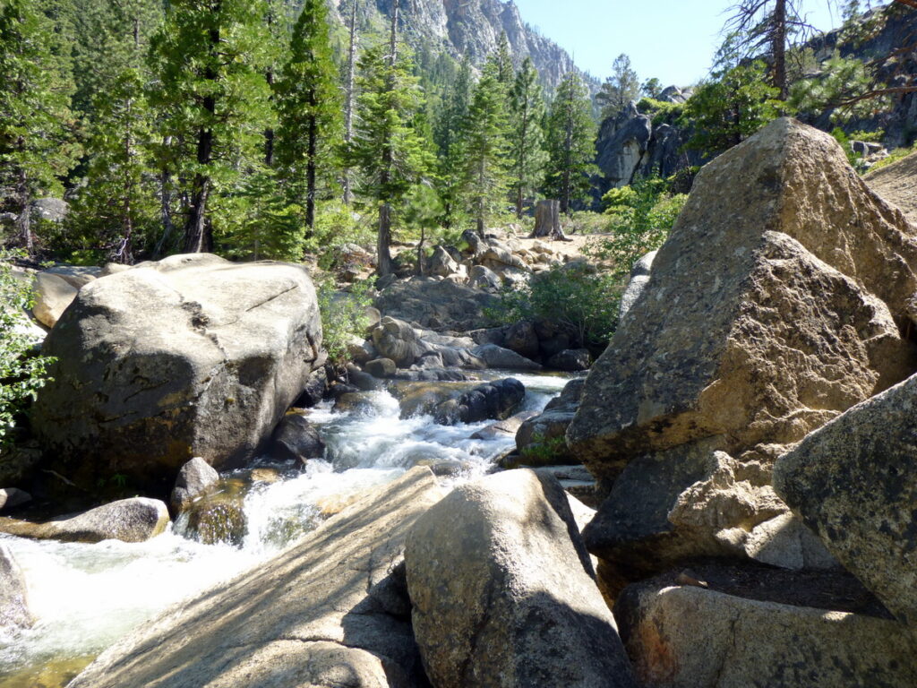 Cascada estrecha encajada entre paredes de roca húmeda en un valle alpino boscoso