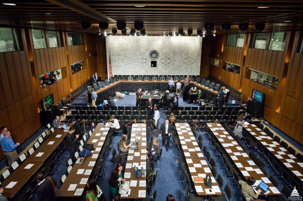 Sala de comisi&oacute;n parlamentaria con estrado curvo, micr&oacute;fonos y asientos vac&iacute;os
